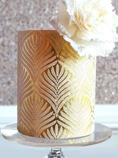 there is a gold and white decorated cake on the table with flowers in it's centerpiece