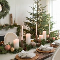 a dining room table set for christmas with candles and greenery