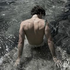 a man sitting in the water with his back turned to the camera and no shirt on