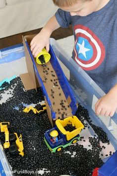 a young boy playing with toys in a plastic container filled with black rocks and gravel