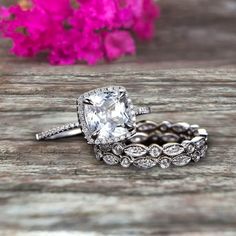 two wedding rings on top of a wooden table with flowers in the backgroud