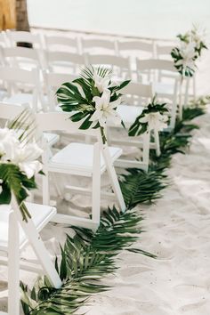 white chairs lined up on the beach with flowers and greenery