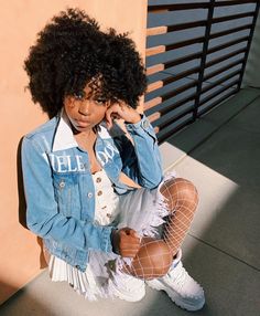 a woman sitting on the ground with her legs crossed, wearing white shoes and denim jacket