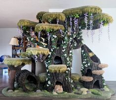 a cat house made out of fake trees and grass with flowers on the roof, in a living room