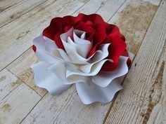 a red and white paper flower sitting on top of a wooden floor next to a piece of wood