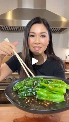 a woman is holding chopsticks over a plate of food with green vegetables on it