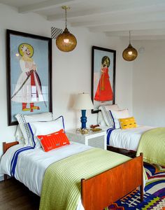 two beds in a room with paintings on the wall and lamps hanging above each bed