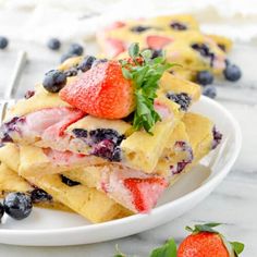 a white plate topped with waffles covered in blueberries and strawberries next to a fork