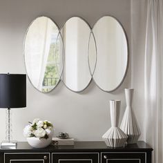 three round mirrors are hanging on the wall above a black dresser with flowers and vases