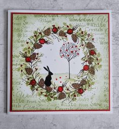 a handmade christmas card with a rabbit sitting in front of a tree, surrounded by pine cones and berries