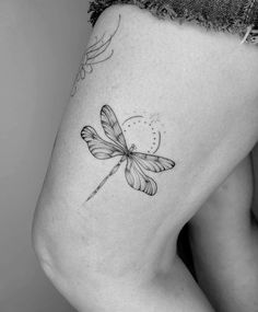 a black and white photo of a woman's thigh with a dragonfly tattoo on it