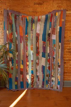 a large multicolored patchwork quilt hanging on a brick wall next to a potted plant