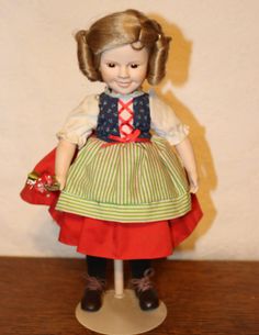 a doll with blonde hair wearing a dress and holding a red purse on top of a wooden table