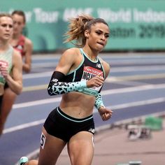 a woman running on a track with other women behind her in sports bras and leg warmers