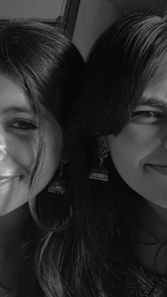 two young women are smiling and posing for the camera, one is wearing large earrings