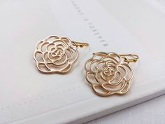 These are pair of beautiful camellia rose earrings. They are made with golden plated over brass flower shaped filigree pendants. The flower is available in two different golden color. The gold color is in a deep gold; and light gold color is in a light gold tone. The earrings measure about 31mm (1.25 inches) from the top of the ear wires to the bottom of the flower. They are perfect for many occasions, gift giving or as a little treat for yourself. Your earrings will presented in a jewelry gift Rose Gold Earrings With Rose Flower Design, Formal Gold Flower Earrings With Rose Design, Gold Rose Design Earrings For Anniversary, Elegant Gold Flower Earrings Nickel Free, Gold Earrings With Rose Design For Gift, Gold Earrings With Rose Design As Gift, Formal Gold Earrings With Rose Design, Rose Gold Flower Earrings With Rose Design, Rose Design Flower Earrings In Rose Gold