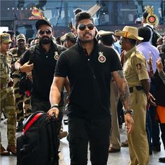 a man in black shirt and sunglasses walking with his luggage near other men wearing army uniforms