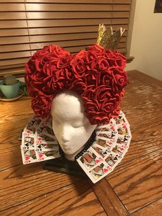 a hat made out of playing cards and roses on top of a wooden table with blinds in the background