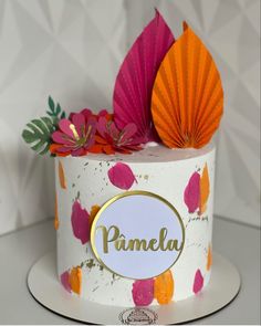 a white cake with pink, orange and yellow decorations on it's top that says pamelu