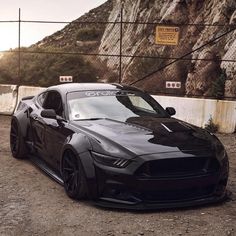 a black sports car parked in front of a fence with mountains in the back ground