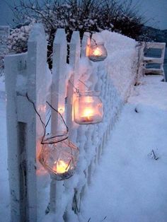 lighted mason jars are lined up on a fence in the snow