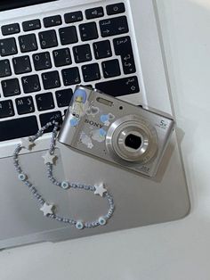 a silver camera sitting on top of a laptop computer next to a rosary and star necklace