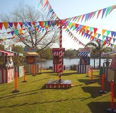 colorful carnival rides are lined up on the grass near water and flags flying in the air