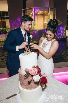 a bride and groom cutting their wedding cake together at the reception table in front of an illuminated background