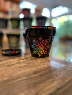 there is a black cup with colorful designs on it sitting on the counter next to other cups