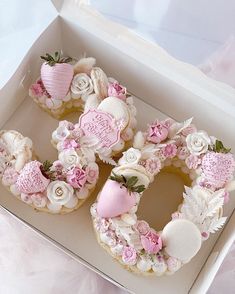 a white box filled with cookies covered in pink and white frosted decorations on top of a table