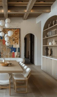 a dining room table with white chairs and a large painting on the wall behind it