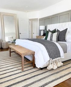 a bedroom with a large bed and white furniture on top of a wooden floor next to a mirror