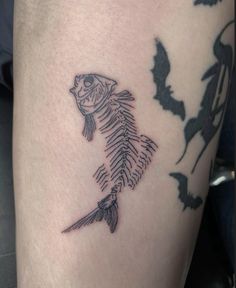 a black and white photo of a fish skeleton tattoo on the right side of the leg