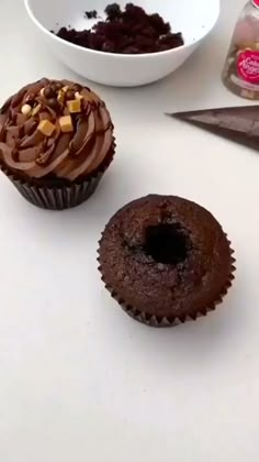 two cupcakes with chocolate frosting and nuts on top, next to a bowl of cookies