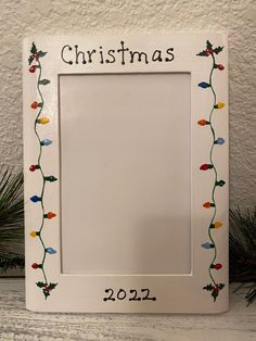 a white christmas frame sitting on top of a table next to pine cones and evergreen branches