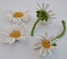 three crocheted white and yellow daisies on a white surface with green stems