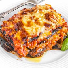 a white plate topped with lasagna covered in cheese and sauce next to a fork