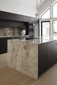 a modern kitchen with marble counter tops and black cabinets, along with wooden flooring