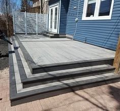 a wooden deck in front of a blue house with steps leading up to the door