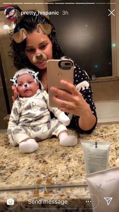 a woman holding a baby and taking a selfie with her cell phone in the mirror