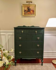 a green dresser sitting next to a lamp on top of a wooden table in a living room