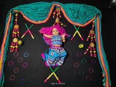 a baby doll laying on top of a black surface with colorful decorations hanging from it's sides