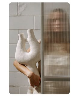 a woman holding a white vase in front of a brick wall