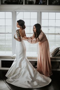 two women standing next to each other in front of a window with tattoos on their arms