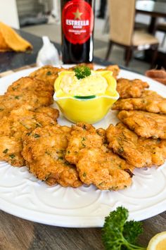 some fried food on a white plate next to a bottle of beer and lemon wedges