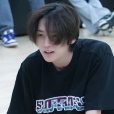 a young man sitting on the floor with his skateboard in front of him and people standing behind him