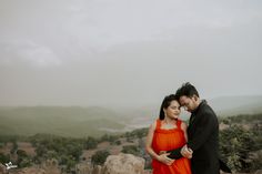 a man and woman standing next to each other on top of a rock covered hillside