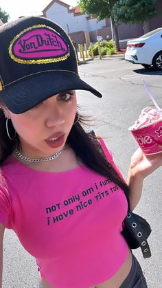 a woman wearing a pink shirt and black hat holding a drink in her right hand