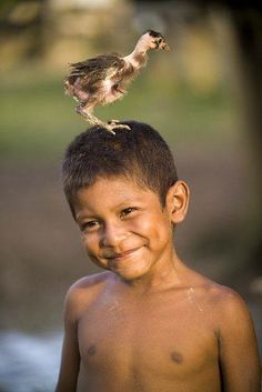 a young boy is smiling and holding a bird on his head while standing next to him