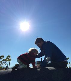 a man kneeling down next to a little boy on top of a rock with the sun in the background